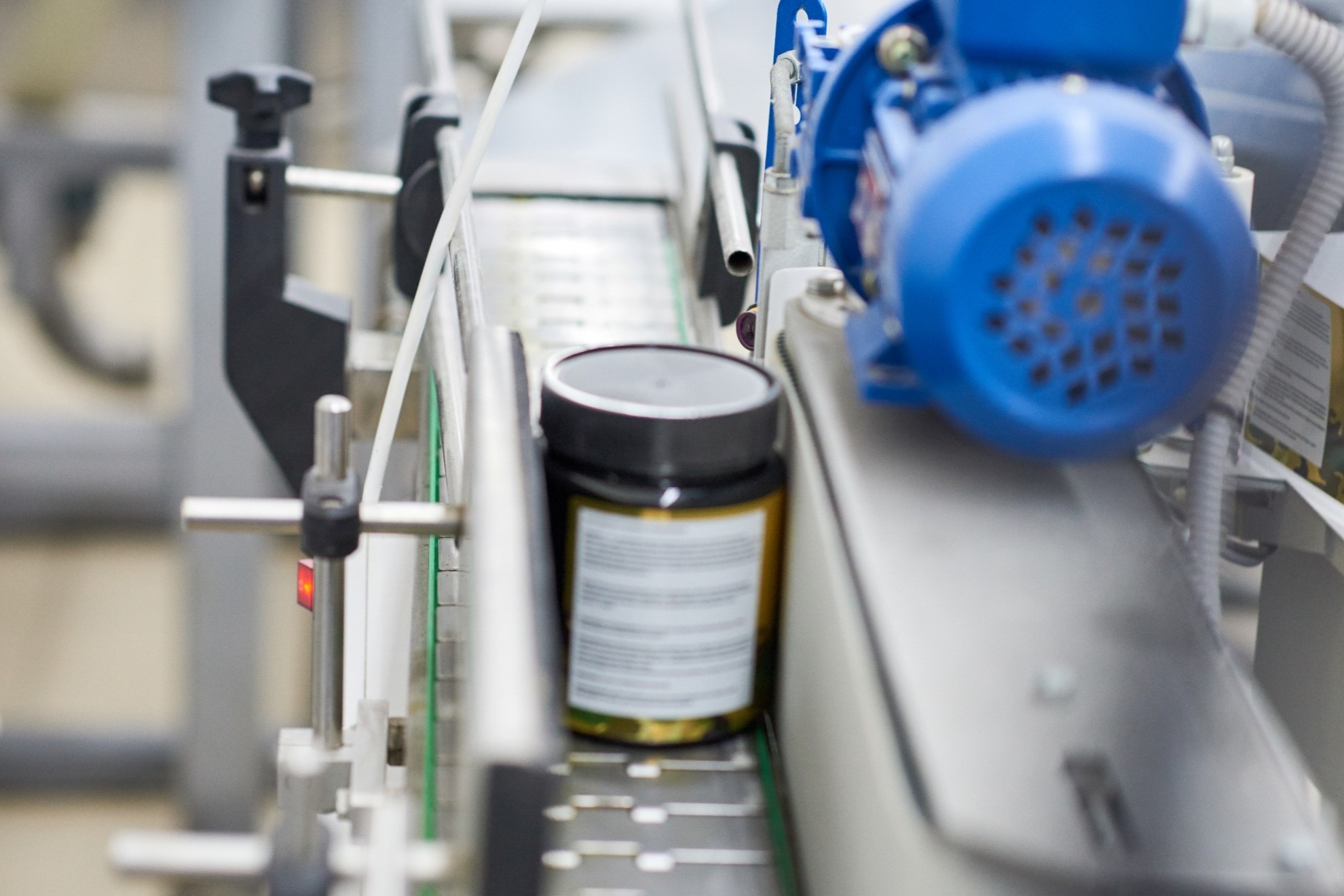 Jar of pharmaceutical product traveling on a conveyor system during automated packaging operations.